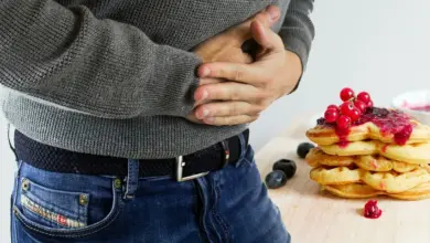 Homem com as mãos sobre o estômago ao lado de um prato de doces, sintoma de gastrite erosiva